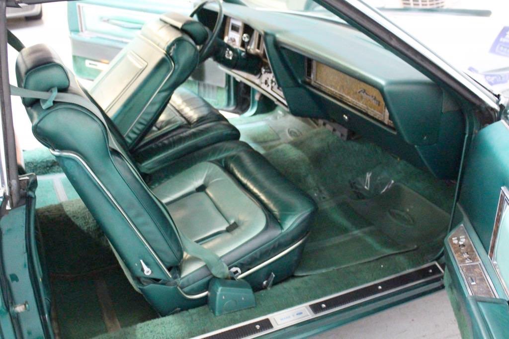 Interior of a vintage car with green leather seats, dashboard, and carpet.