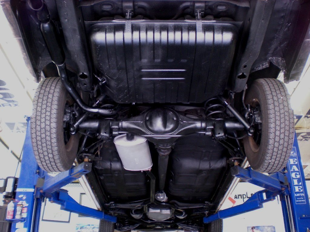 Underneath the raised vehicle showing the front suspension, oil pan, and exhaust system on a hydraulic lift.