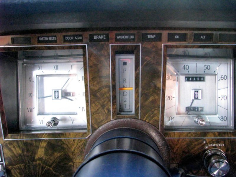 Dashboard of a vintage car with clock, speedometer, gear shift indicators, and various controls.