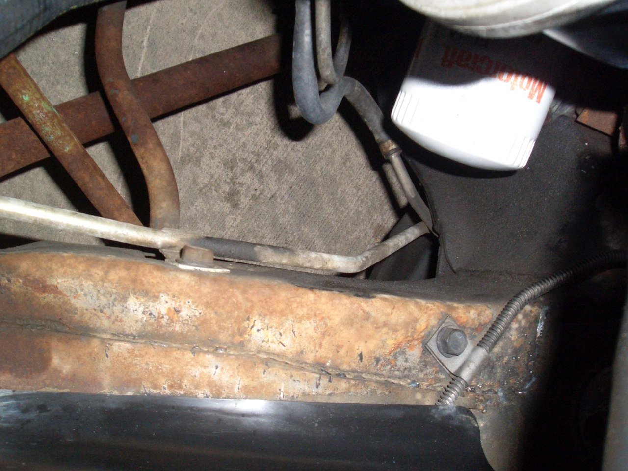 Close-up of rusty metal framework and tubing, with a partially visible bottle and some wiring.