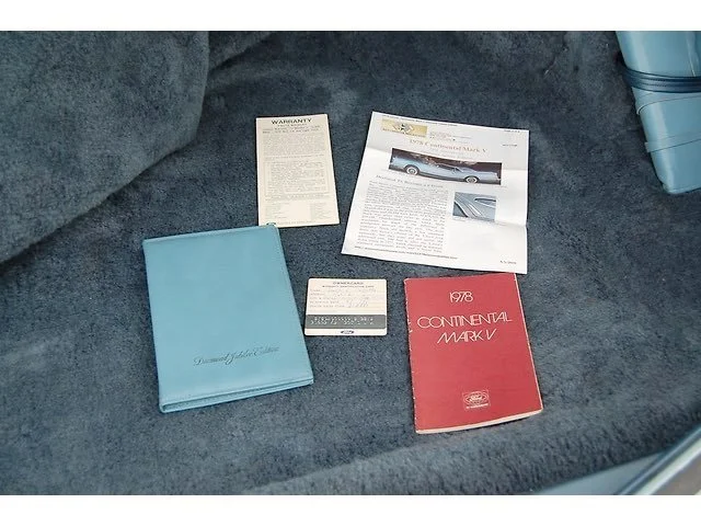 Car manual, warranty papers, car brochure, and a small beige card on a car seat.