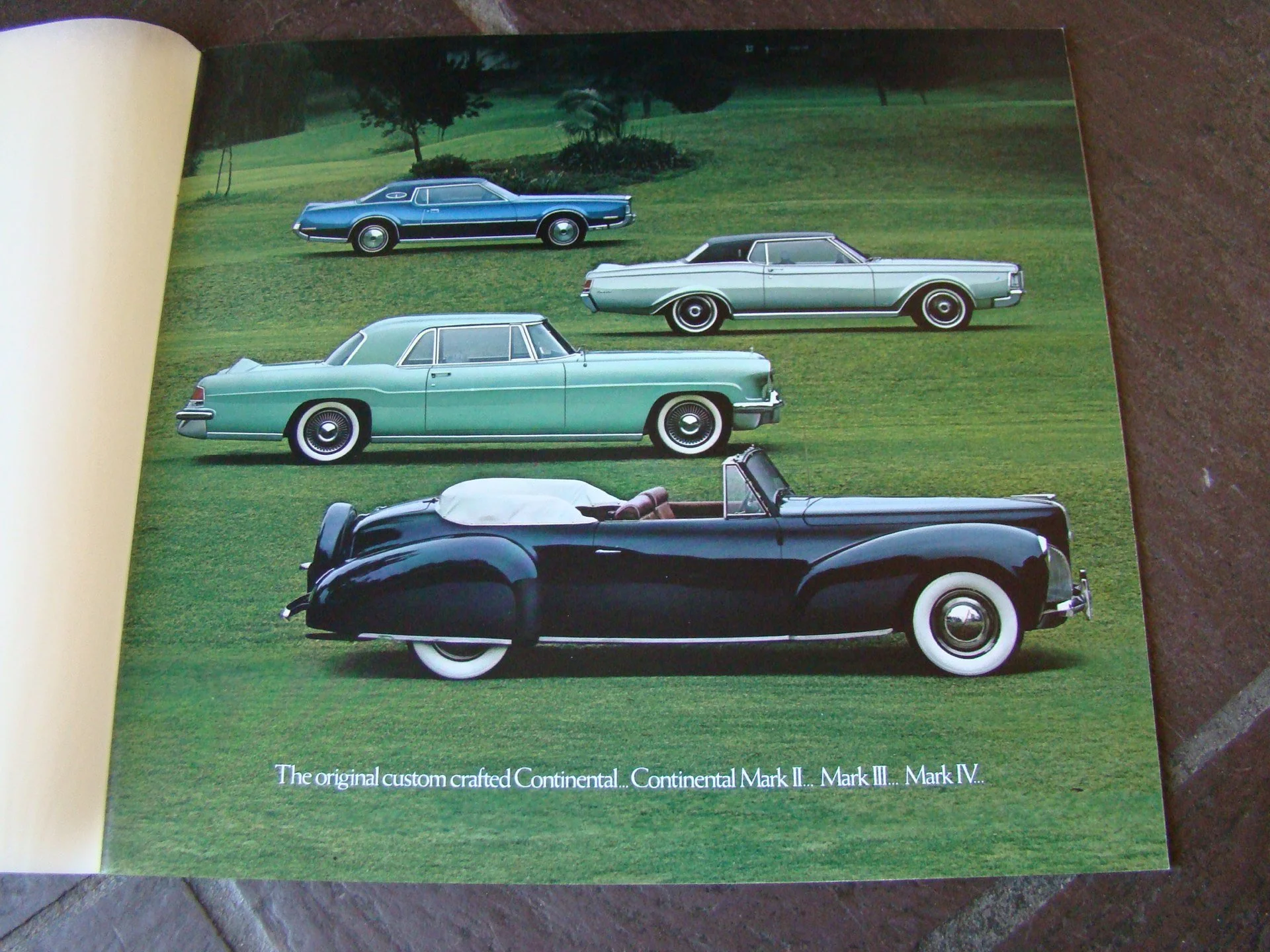 Historical photo of five vintage cars parked on grass, with trees in the background. The cars are a blue coupe, a silver coupe, a mint green sedan, a black convertible with whitewalls, and a small white convertible in the back. Caption reads, 'The or