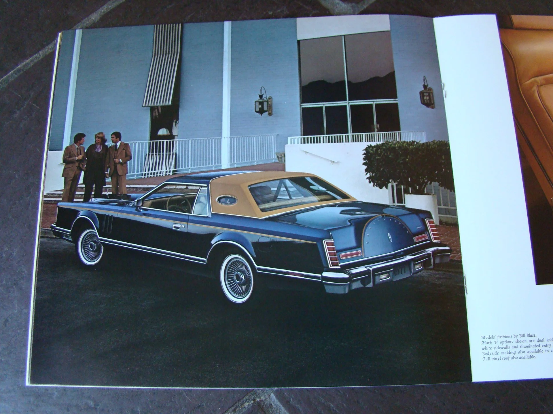 A vintage black car with a beige roof parked outdoors in front of a building with three men dressed in suits standing nearby.