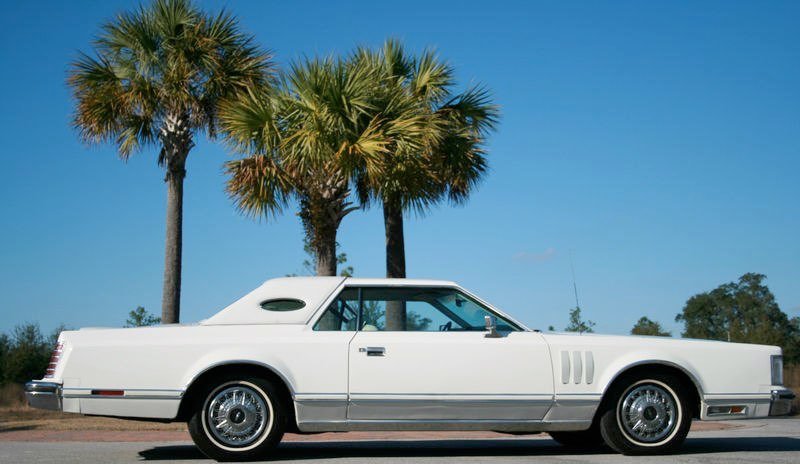 A vintage white convertible car parked under palm trees on a sunny day.