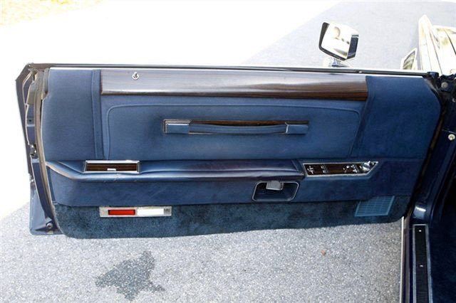 Close-up of a vintage car's blue interior door panel, featuring a wood trim, window controls, and a door handle.