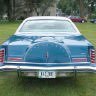 Rear view of a blue classic car parked on grass with trees in the background