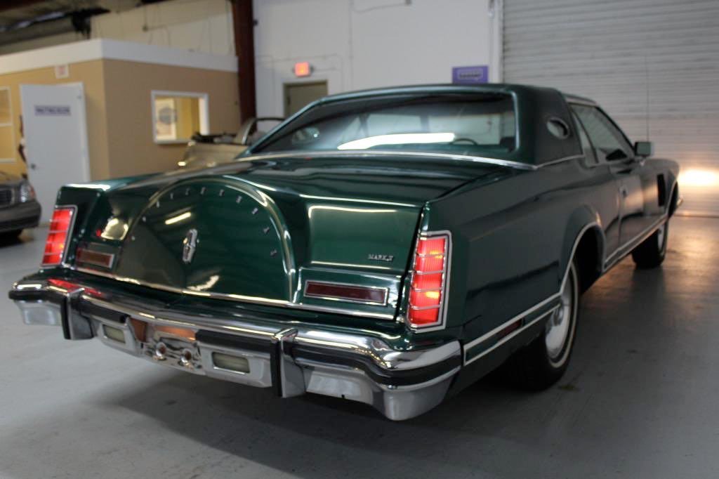 Green classic car with chrome bumper and taillights, parked indoors in a garage.