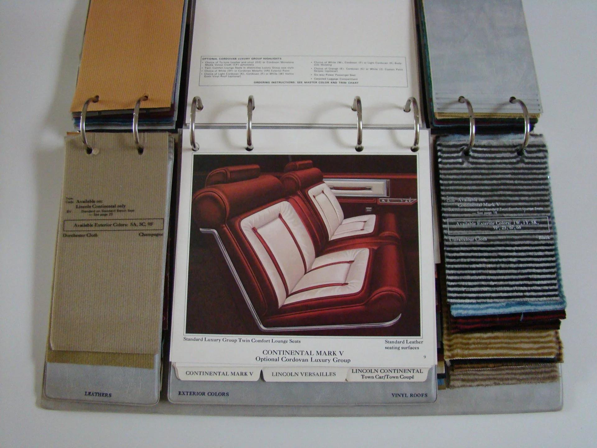 Color swatches, fabric samples, and a page with an image of a luxury car interior, including red and white upholstered seats and decor, displayed in a binder.