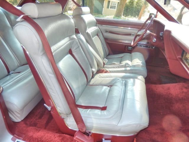 Interior of a vintage car with white leather seats and red seat belts on red carpet.