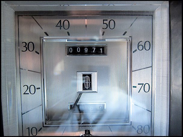Close-up of a mechanical odometer showing 971 miles, with a background of a speedometer gauge marked from 0 to 80.