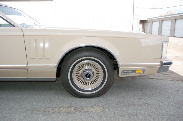 Close-up of the front half of a vintage beige luxury car, showing the wheel, side panel, and part of the door.