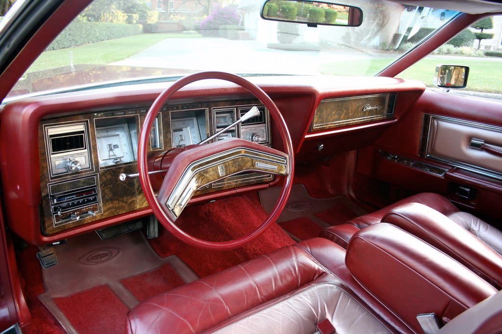 Interior of a vintage red car with a dashboard, steering wheel, and leather seats.