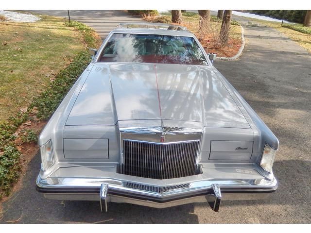 Front view of a vintage silver Cadillac Eldorado parked on a paved area with trees and shrubs nearby.