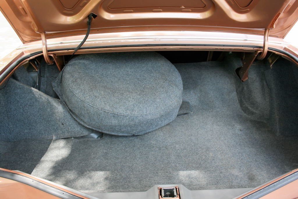 The open trunk of a car showing gray carpeted interior and a spare tire with a fabric cover.