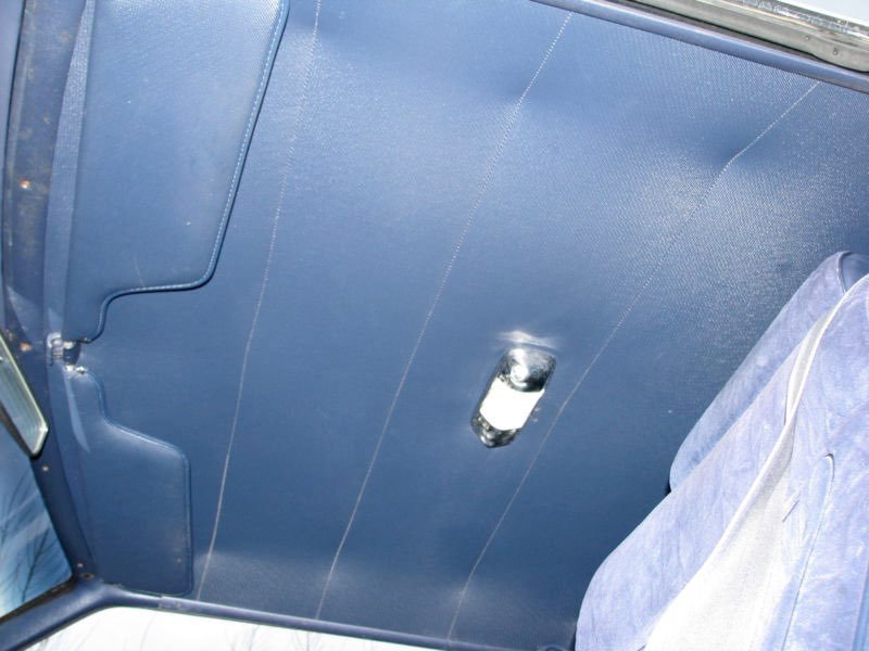 Interior of a vehicle with blue headliner and a small chrome mirror attached to the ceiling.