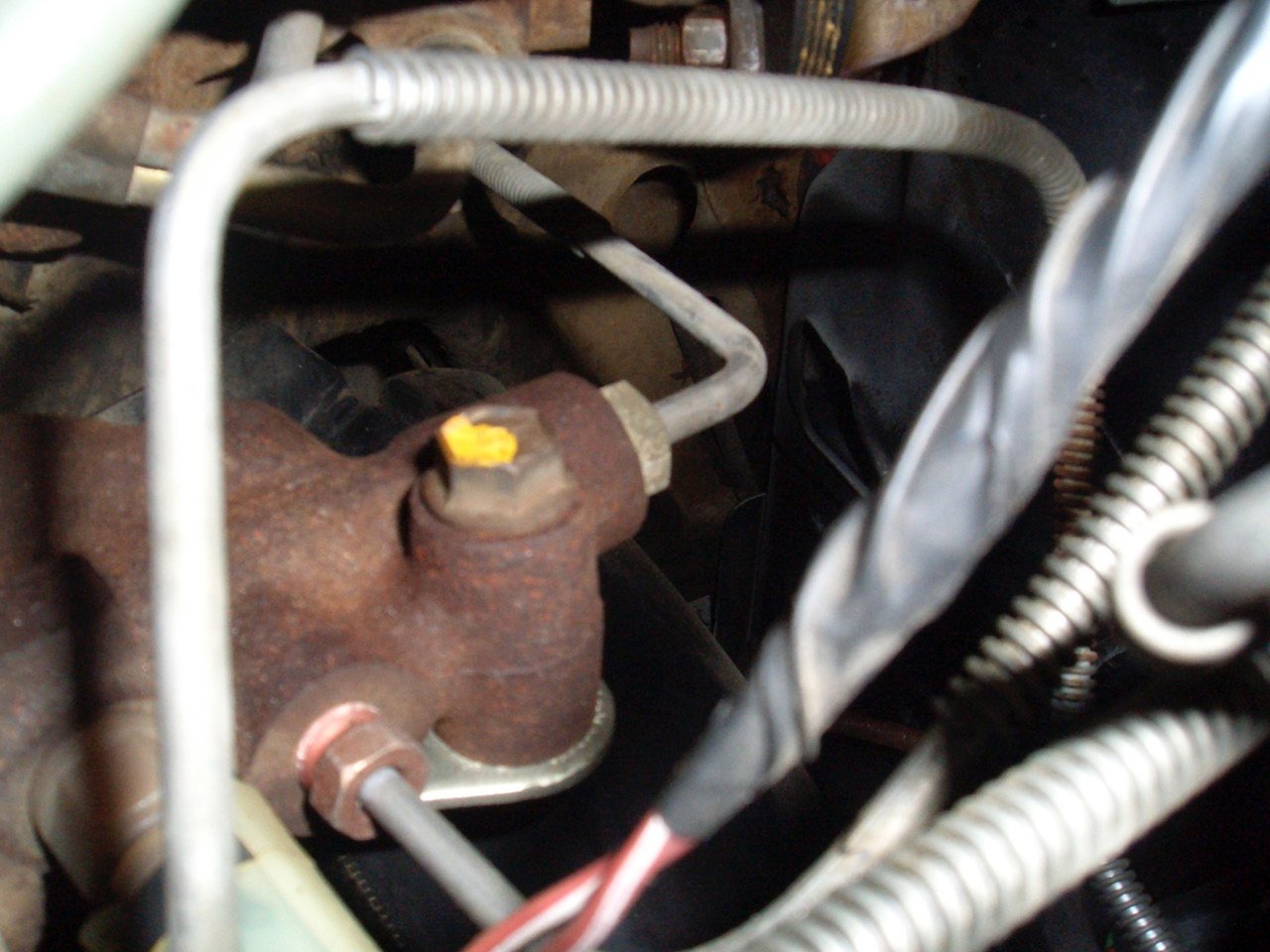 Close-up of a rusted fuel pressure regulator with attached metal lines and wiring inside a vehicle engine compartment.