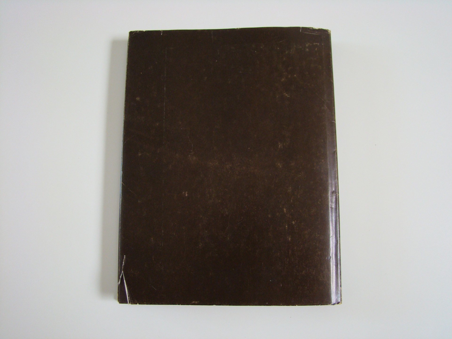 A worn dark brown hardcover book with torn bottom left corner, lying on a white surface