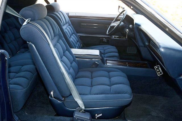 Interior of a vintage car with blue fabric seats, a black dashboard, and a steering wheel.