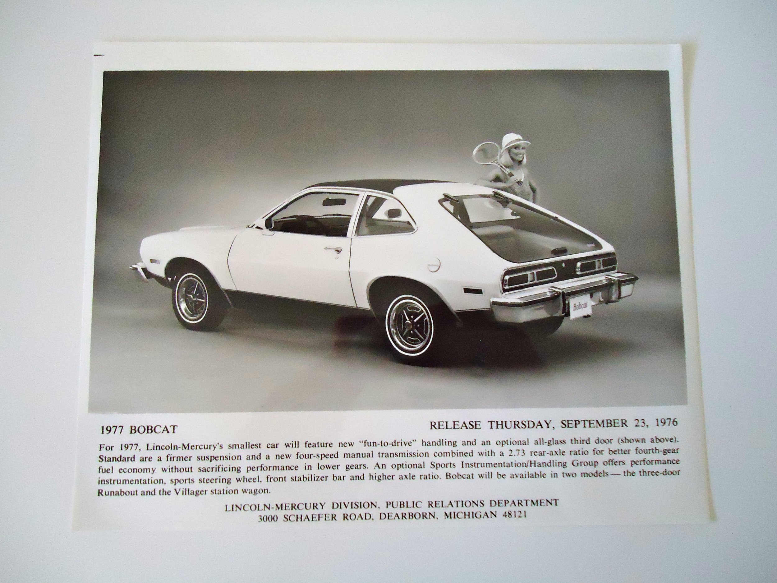 Black and white promotional photo of the 1977 Lincoln Mercury Bobcat car with a woman holding tennis rackets and wearing a visor standing behind it.