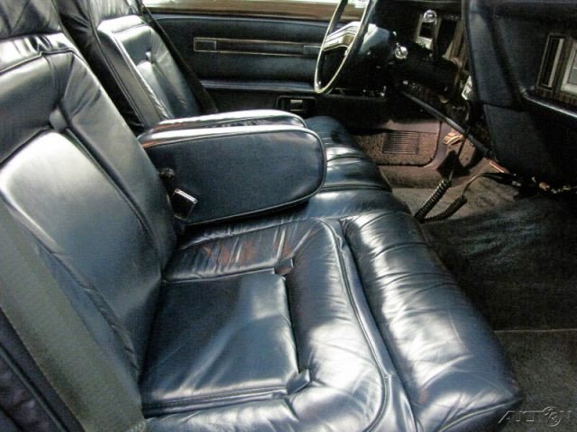 Interior of a vehicle showing black leather front seats, with a center armrest, and part of the steering wheel and dashboard visible.