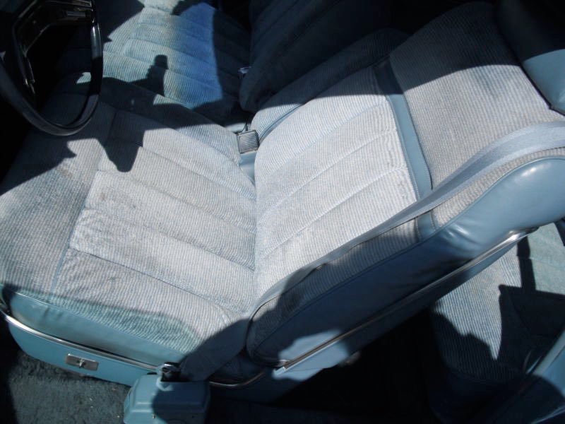 Inside of a car showing the front passenger seat and part of the driver’s seat, both with light-colored fabric upholstery.