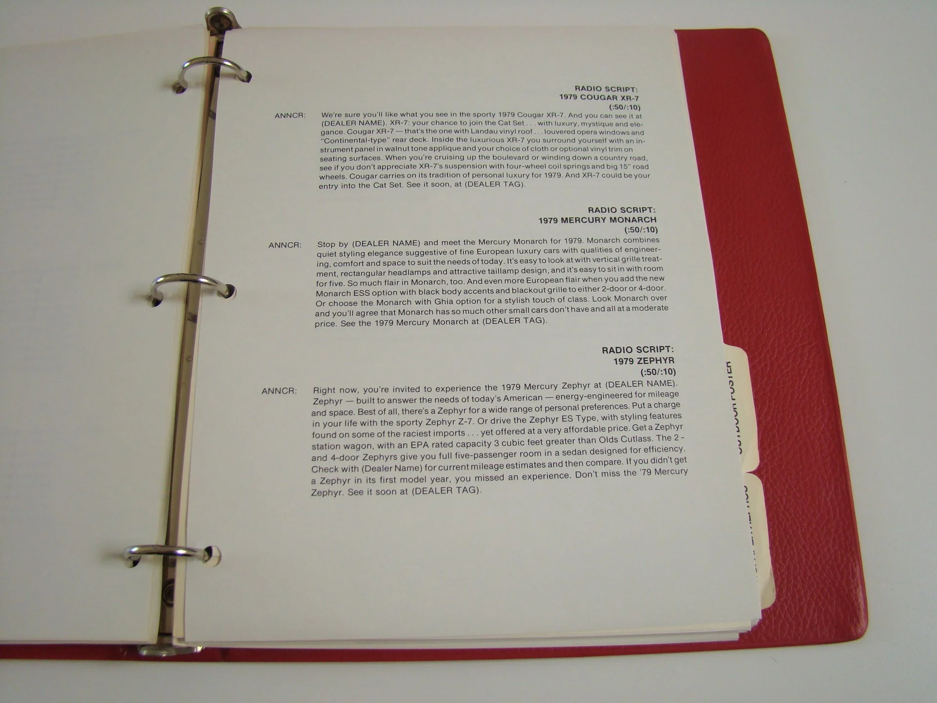 Open binder with white pages containing text about various car models and radio scripts, with a red textured cover visible on the right side.