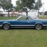 A classic blue convertible car parked on a grassy area.