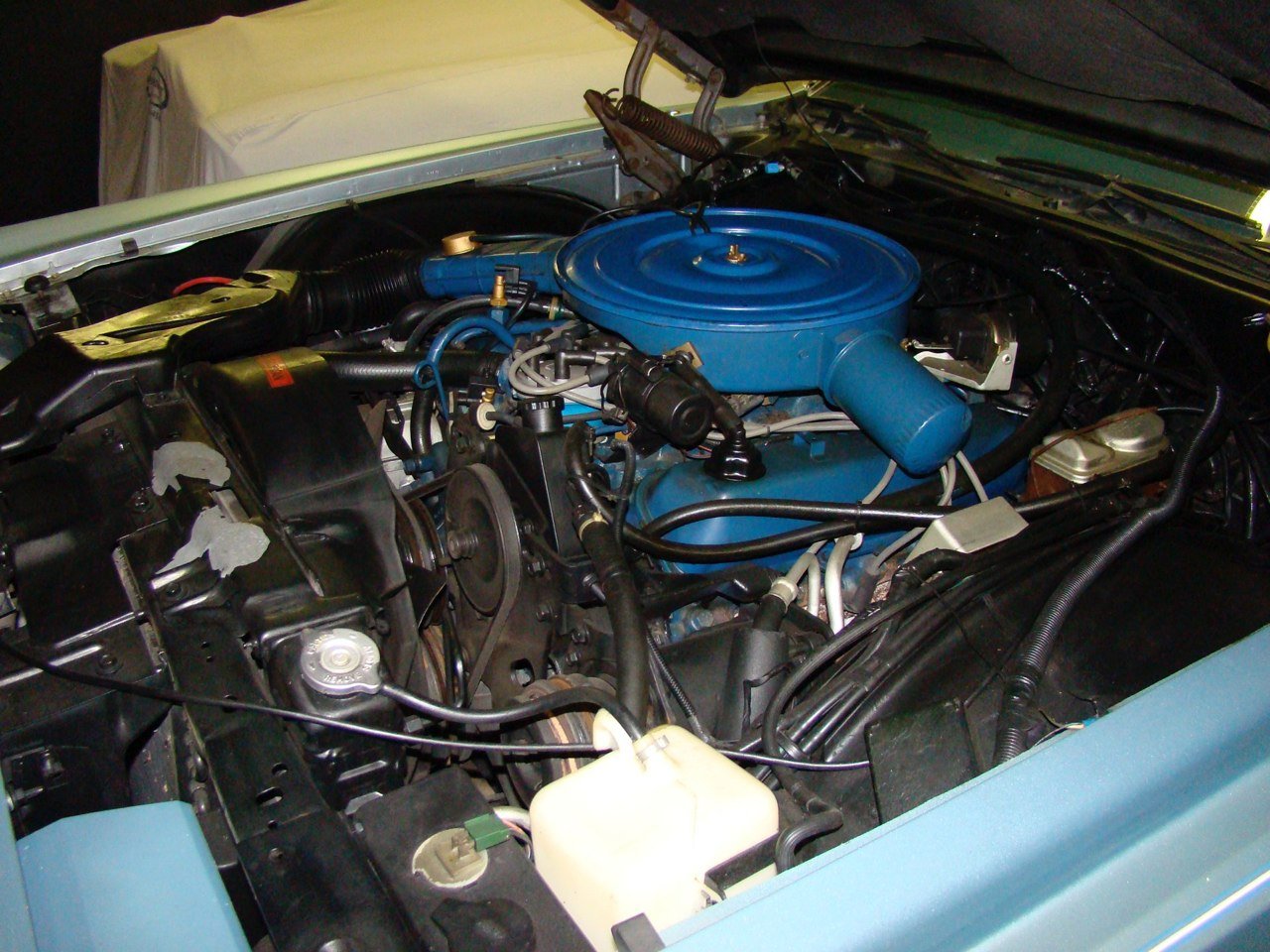 Close-up of a classic car engine with a blue air cleaner cover and various black, blue, and white engine components.