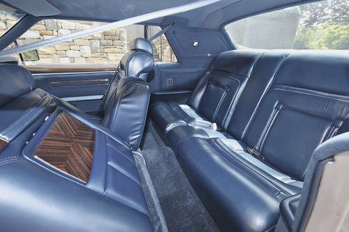 The interior of a vintage car with black leather seats and wood trim on the side panel.