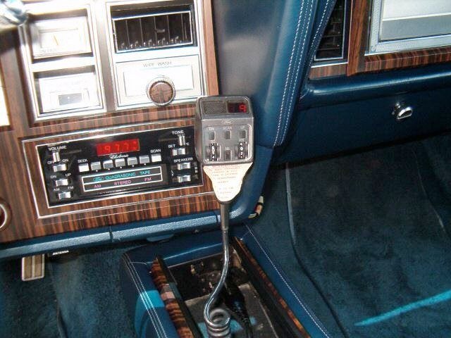 Close-up of a vintage car dashboard with a radio, control panel, and a smartphone mounted on the center console.