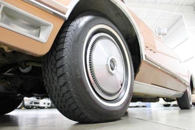 Close-up of a vintage car tire and wheel, with part of the beige body visible, parked indoors.