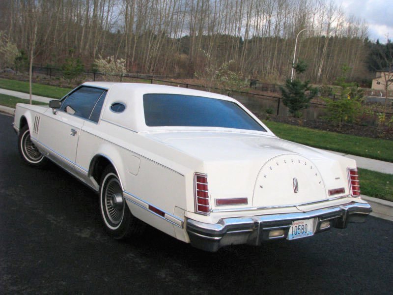 A white vintage Lincoln Continental coupe parked on a street overlooking a park and trees.