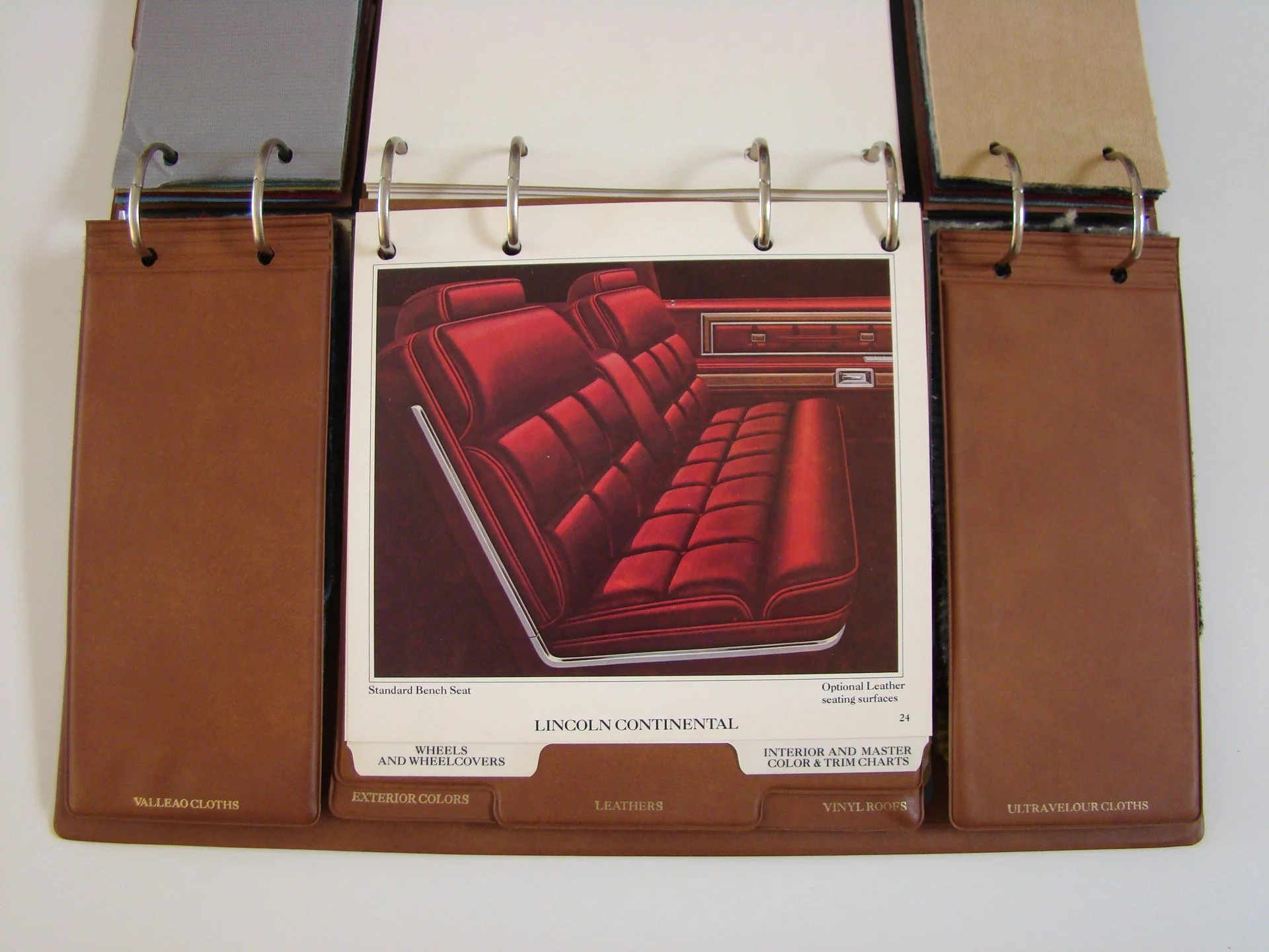 A color sample and fabric swatch binder opened to a page showing a red upholstered car bench seat with labeled options for Lincoln Continental interior design.