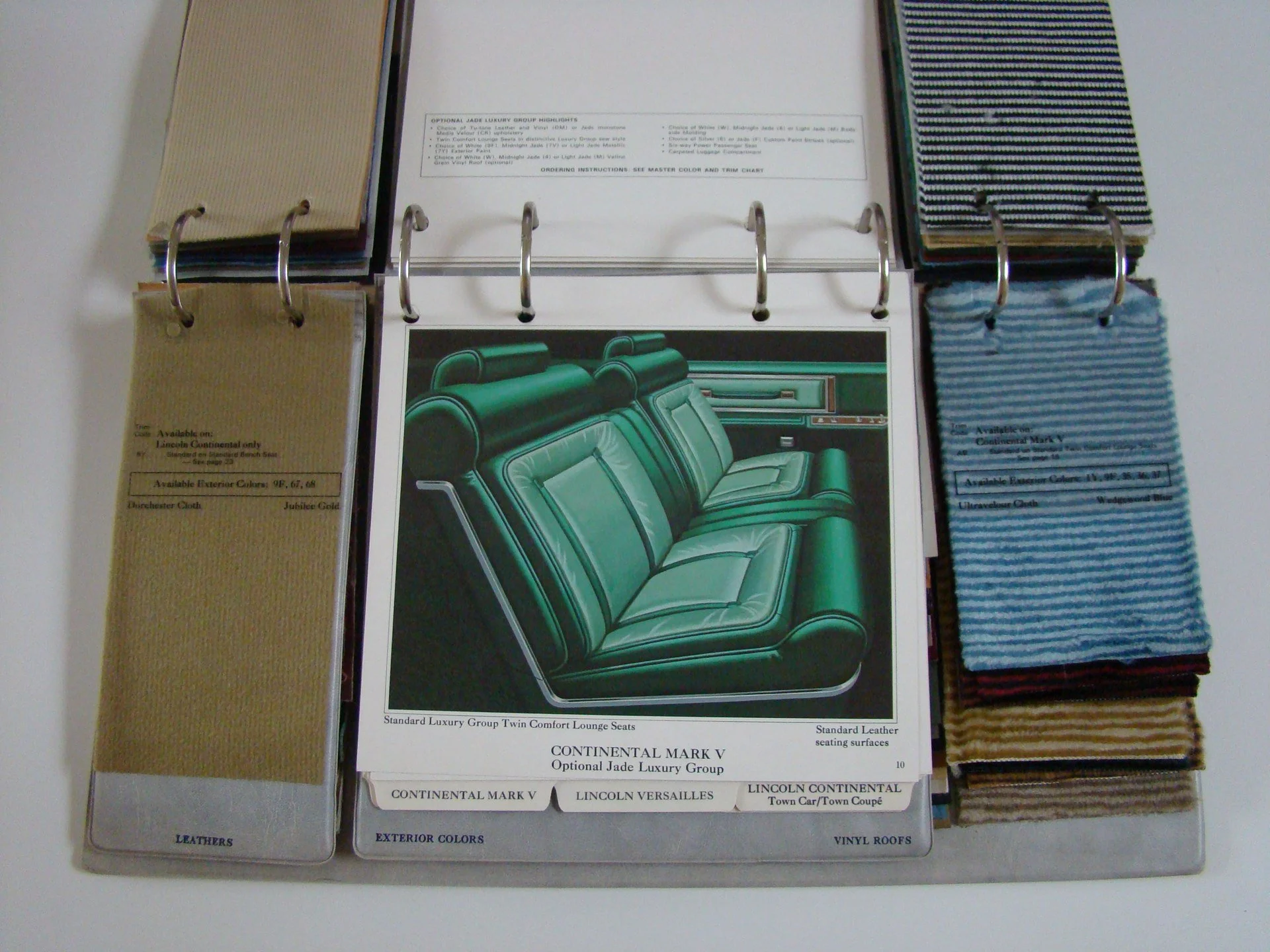 A color sample book showing fabric swatches and a printed interior design plan for a car, including green leather seats.