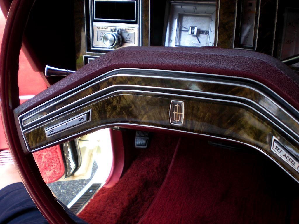 Dashboard and steering column of a vintage Lincoln car with woodgrain accents, switches, and dials.