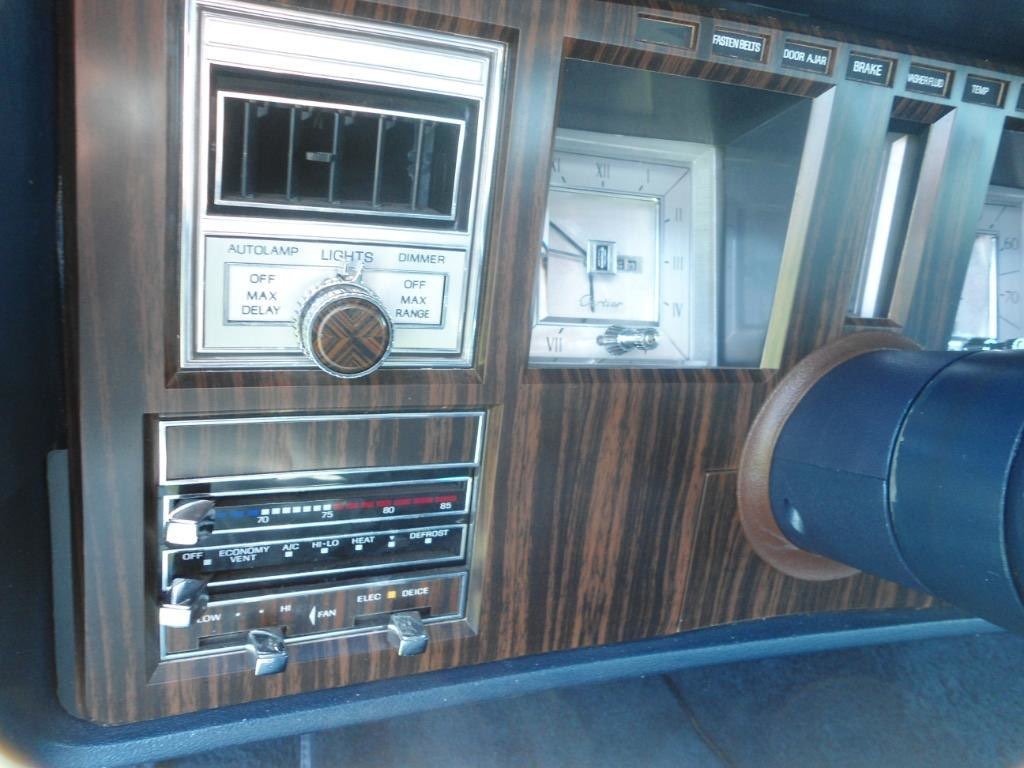 Close-up of vintage car dashboard with wood paneling, featuring climate controls, a clock, and labeled switches.