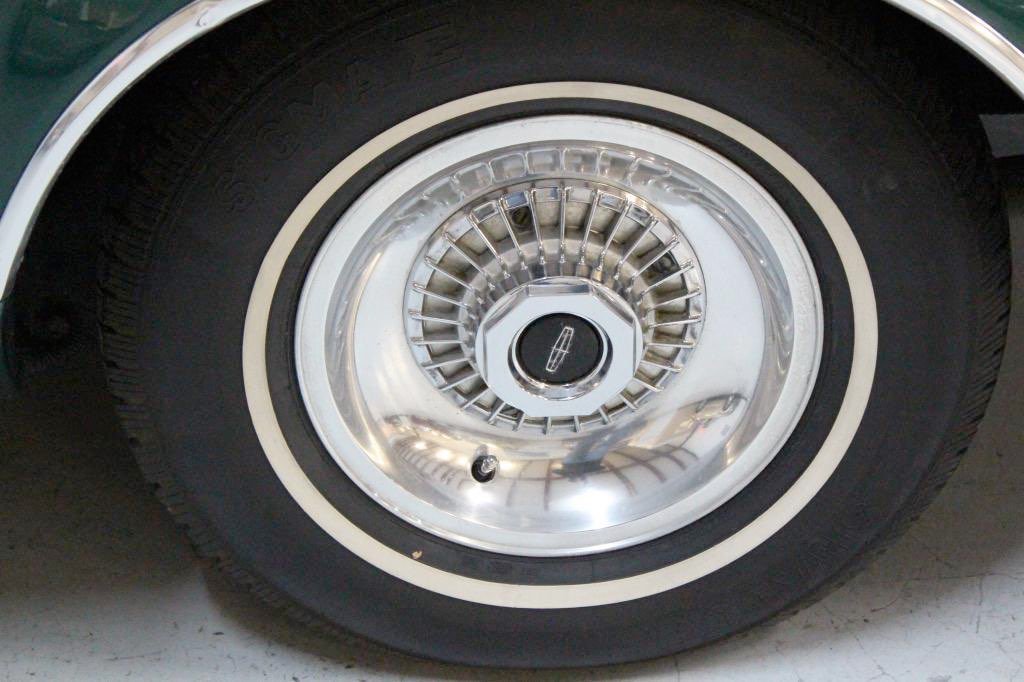 Close-up of a vintage car wheel with chrome hubcap and whitewall tire.