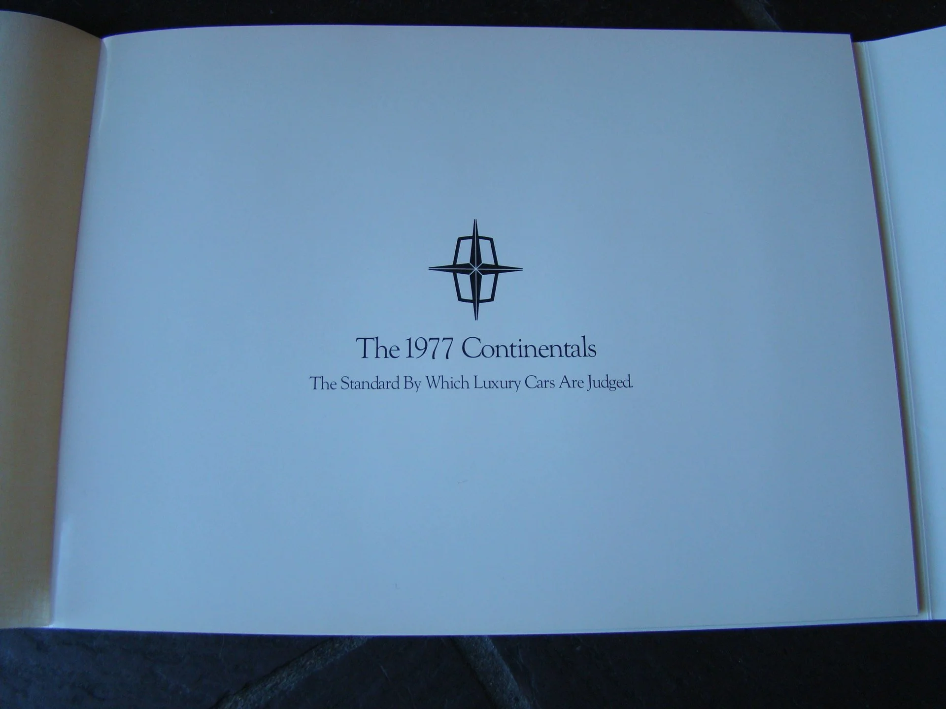 Inside a book with a logo at the top and text that reads 'The 1977 Continentals, The Standard By Which Luxury Cars Are Judged.'
