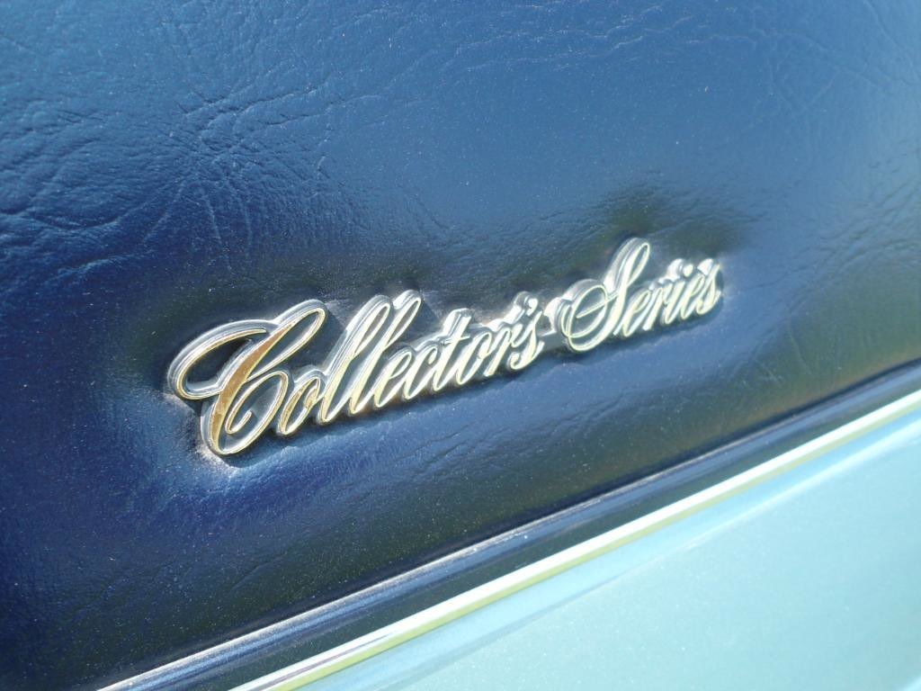 Close-up of a vintage car badge reading "Collector's Series" in silver, mounted on a blue leather surface with a slight shine.