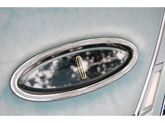 Close-up of an oval car side mirror with a chrome border, reflecting trees, and the inscription 'Diamond Jubilee Styling' on the mirror surface.