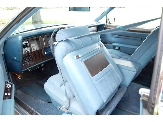 Interior of a vintage car with light blue seats, dashboard, and door panels, featuring a woodgrain dashboard and a rearview mirror.