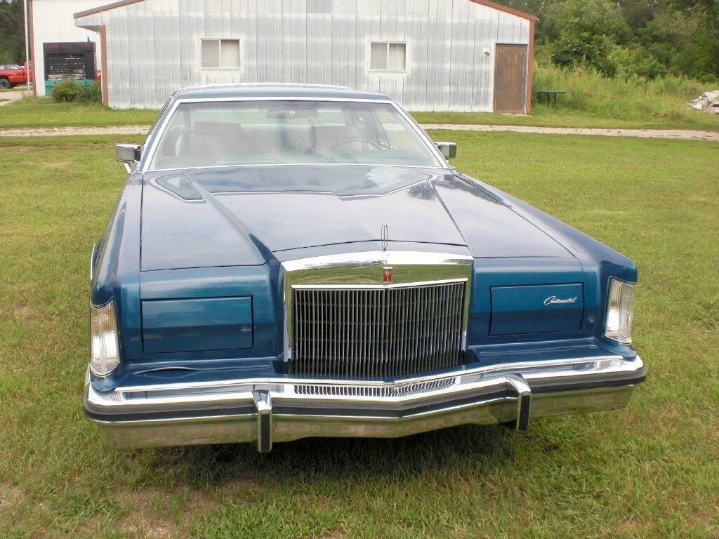 Front view of a vintage blue Cadillac car parked on grass near a barn.