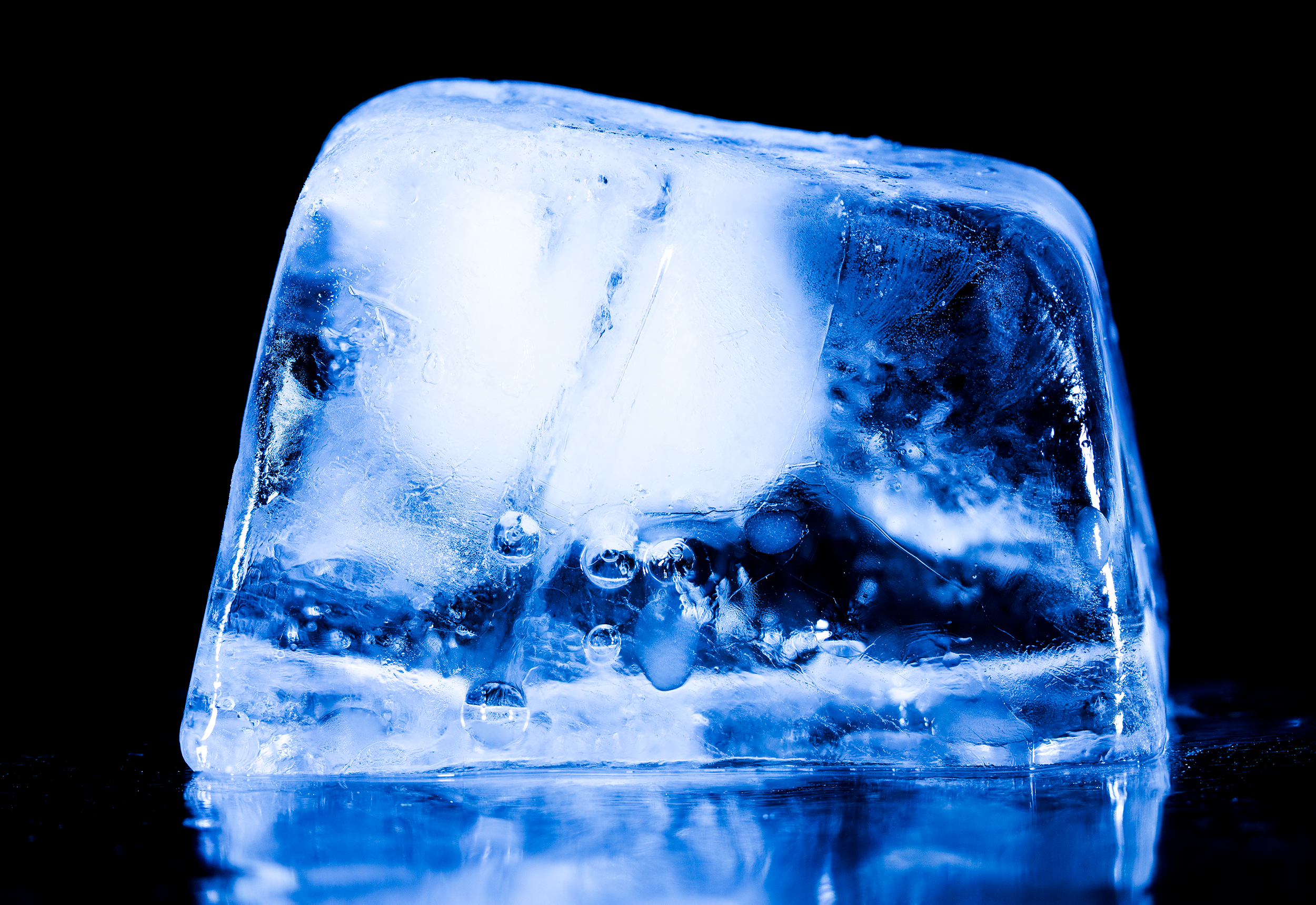 Close-up of a blue-lit ice cube with trapped air bubbles on a dark background.