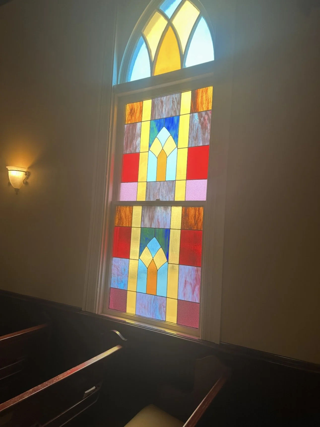Colorful stained glass window with geometric patterns, located in a church or chapel, with wooden pews and soft lighting.