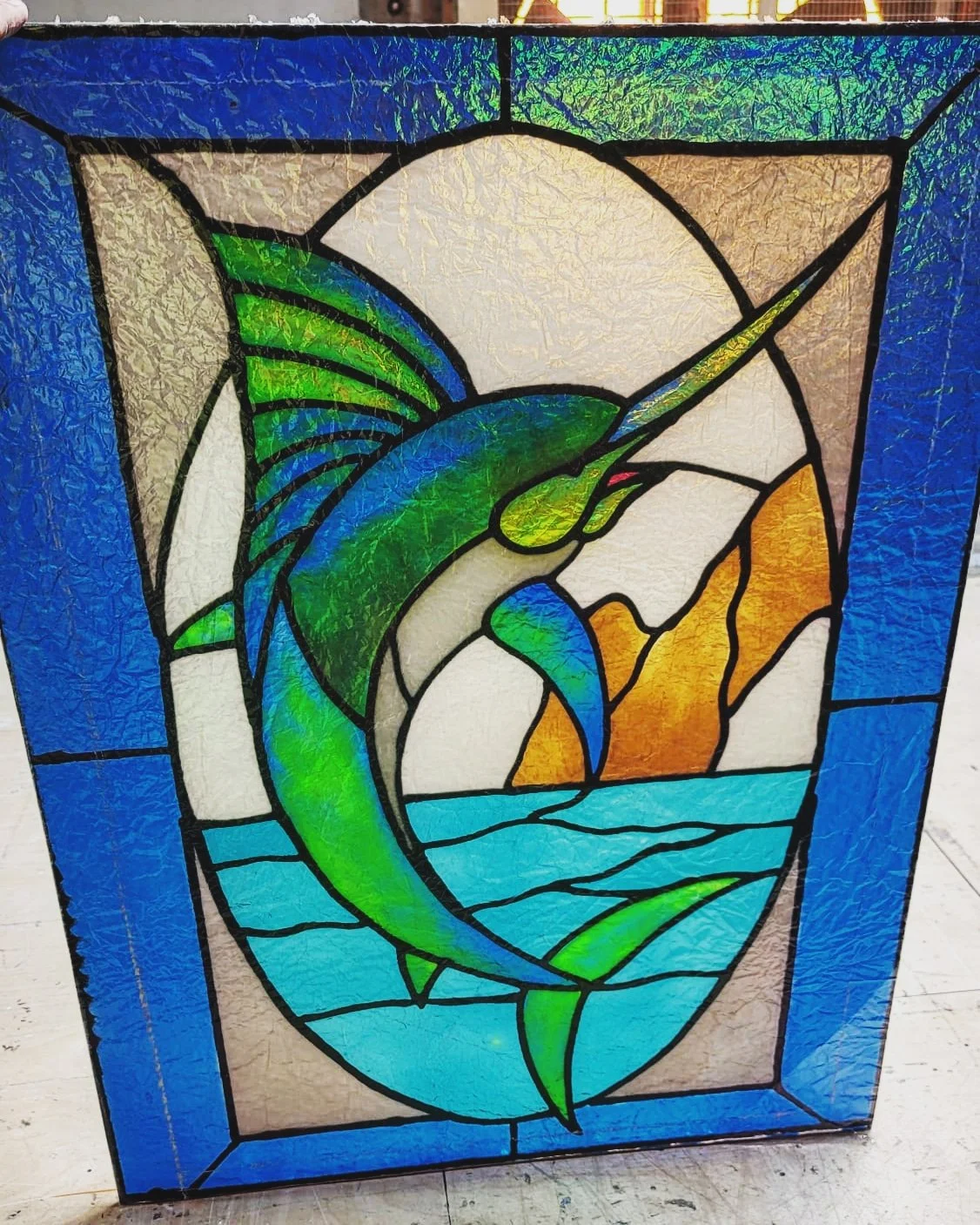 Colorful stained glass window with a dolphin jumping out of water against a sunset background.