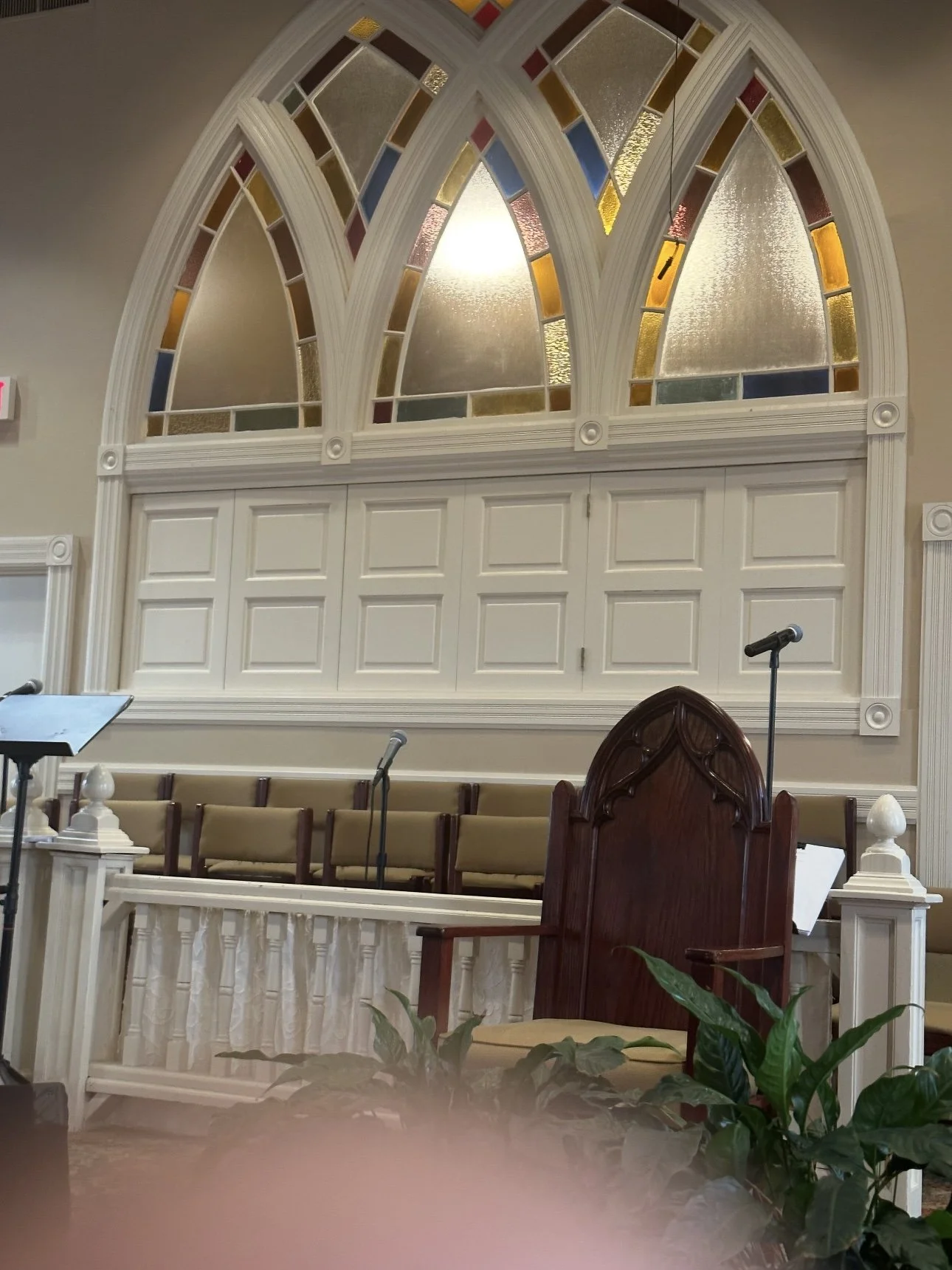 Interior of a church or chapel with white walls, stained glass windows, a wooden pulpit, and a row of chairs.