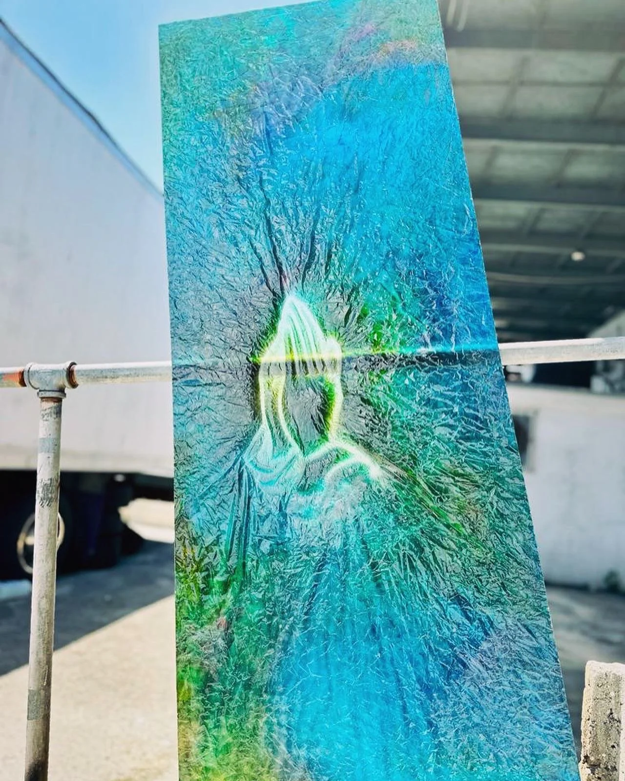 A large sheet of glass with a crack and some colorful reflections, positioned outdoors near a street or parking lot.