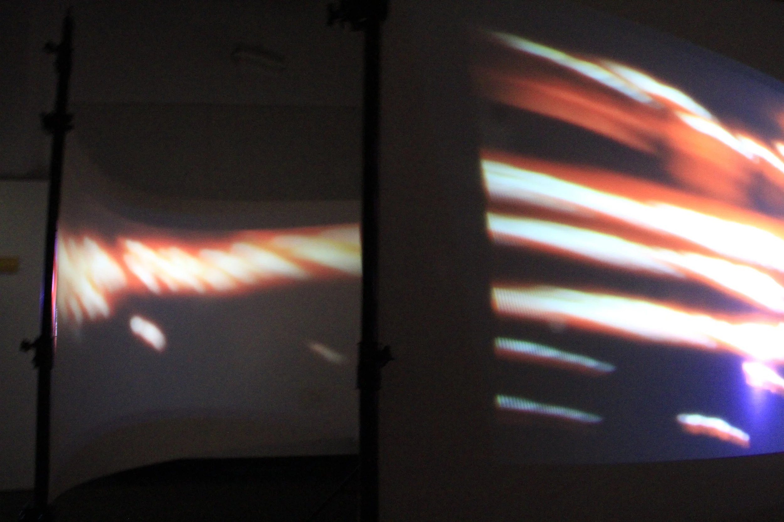 Two projection screens displaying abstract, colorful light streaks with dark surrounding areas.