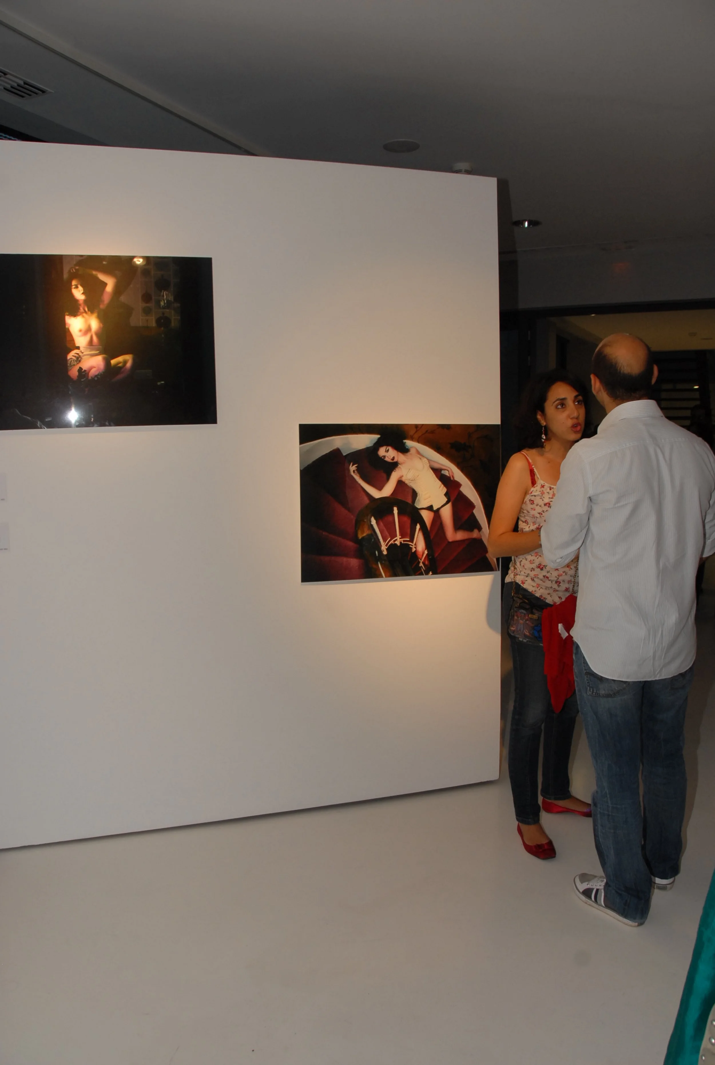 Two people are having a conversation in front of an art display at an art gallery. The display includes two photographs featuring a woman in various poses.