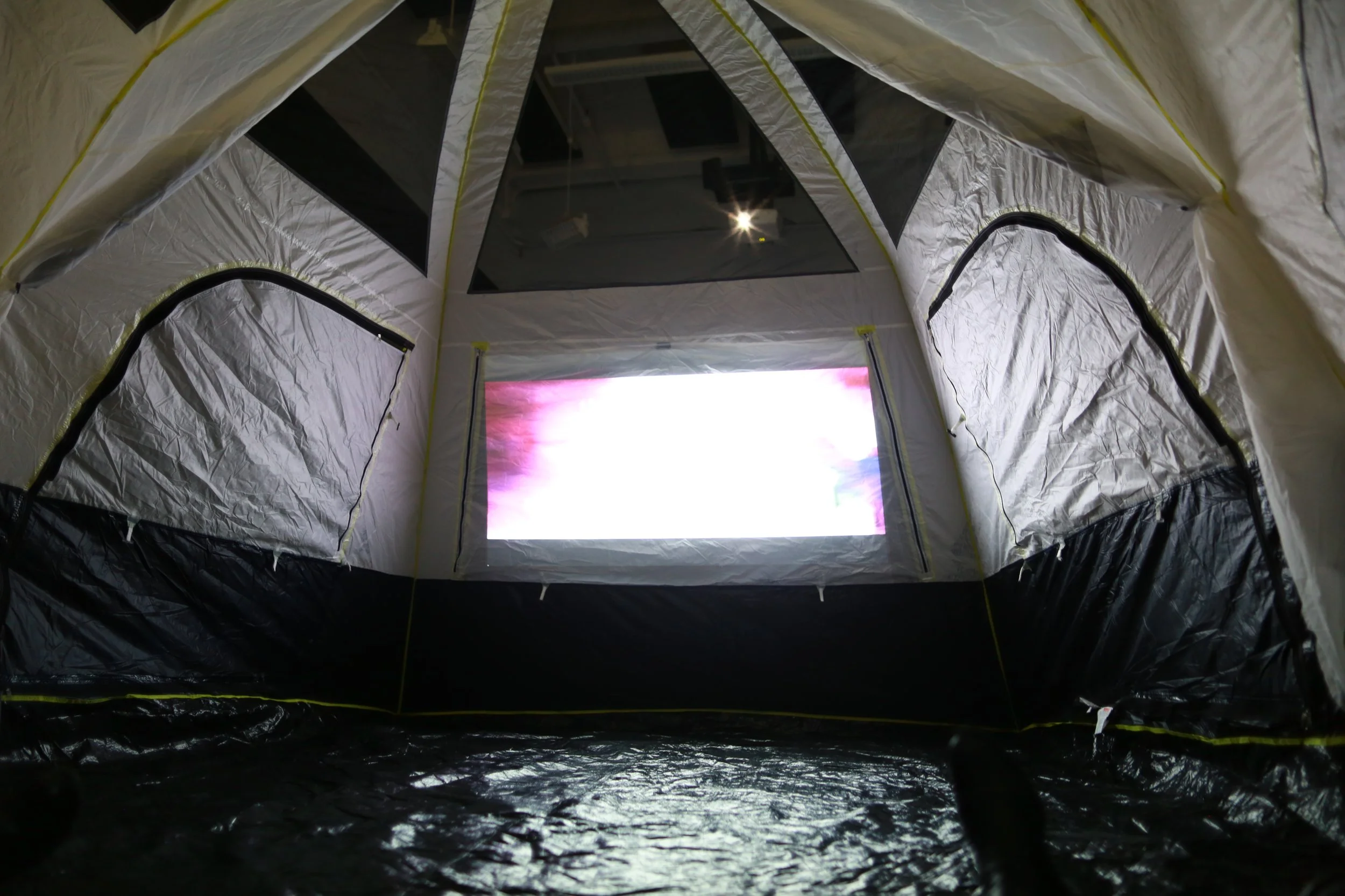 Inside a large, insulated tent with a screen displaying a colorful image, viewed from the ground level.